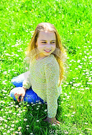 Girl sits on grass at grassplot, green background. Heyday concept. Girl on smiling face spend leisure outdoors. Child Stock Photo