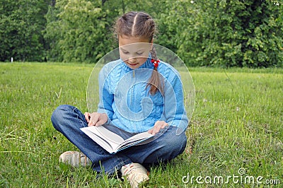 Girl sits on green field and reads book Stock Photo