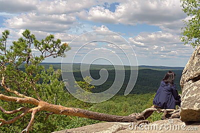 The girl sits on a horizontally growing pine tree on the edge of a cliff Stock Photo