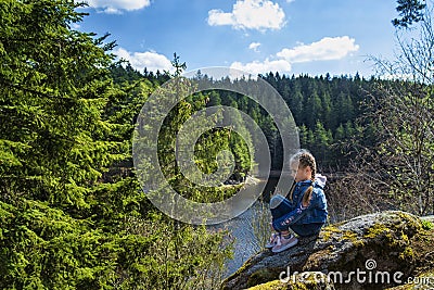 A girl sits in a park near a recreation area in nature. A girl looks from a height at the river.A young girl stands near a cliff, Stock Photo