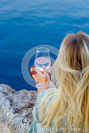 A girl sits on the seashore with glass in her hands. Stock Photo