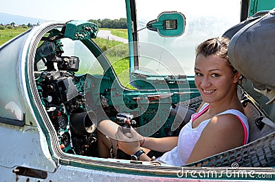Girl sits and smiles in cabin of old jet fighter MiG-21 holding the control stick Editorial Stock Photo