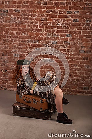 Girl sits on a suitcase in an army dress Stock Photo