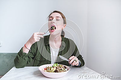 girl sits at the table and eats a salad with a fork. The girl bites green salad and gets plucked Stock Photo