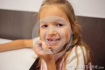 A girl sits at a table and holds in her hands a newly dropped milk tooth. Teeth change in children Stock Photo