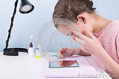 The girl sits at the table, looks in the mirror and changes the contact lens to improve vision Stock Photo