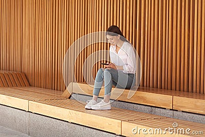 The girl sits on a wooden bench and receives good news. The student is.corresponding with a friend. Woman has an idea and she Stock Photo