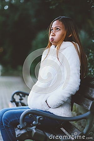 Girl sitting on bench in the city park in cold weather Stock Photo