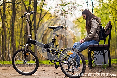 The girl is sitting on the bench and there is a bicycle in front of her Stock Photo