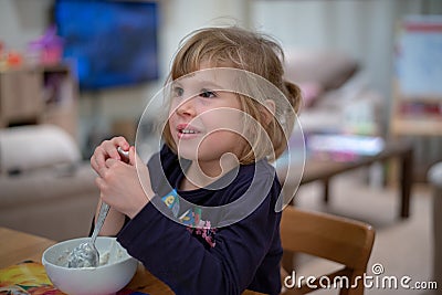 Girl sitting at breakfast eating muesli with yoghourt from white bowl Stock Photo