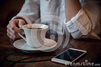 Girl sitting in a cafe in a white shirt with a cup of coffee and a telephone Stock Photo