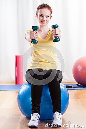 Girl sitting on exercise ball and lifting weights Stock Photo