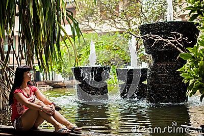 Girl sitting in an exotic Park among the fountains. Travel concept. Back view. woman looking at waterfall in the hotel Stock Photo