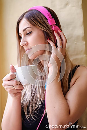 Girl sitting near the window and drinking coffee. single woman in pink headphones and a black tank top. Stock Photo