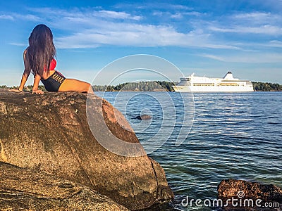 Girl sitting on rock by shore watching passing ship Editorial Stock Photo