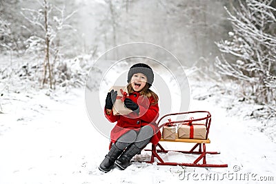 A girl is sitting on a sled in a winter forest with a Christmas gift Stock Photo