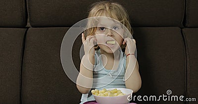 Girl sitting on sofa and eating corn puffs. Child taste puffcorns Stock Photo