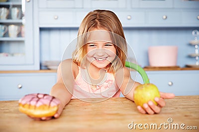 Girl Sitting At Table Choosing Cakes Or Apple For Snack Stock Photo
