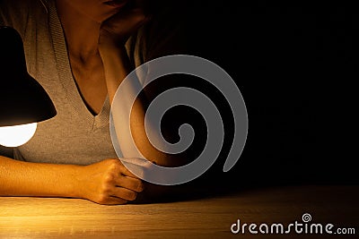 Girl sitting at a table in the light of a table lamp in the dark Stock Photo