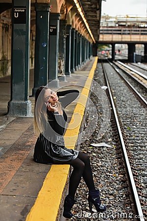 Girl sitting on the train platform while talking on phone. Editorial Stock Photo