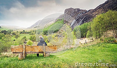 A girl sitting on the wooden bench and looking at the waterfall in Kenmare Stock Photo