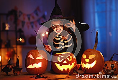 Little girl in witch hat and skeleton costume with magic wand in hand with frightening face Stock Photo
