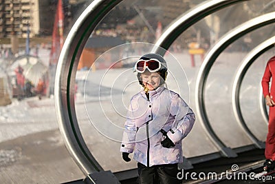 A girl on skis stands on a carpet ski lift in a glass tunel Stock Photo