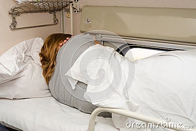 The girl sleeps on top shelf of the side seats in the second-class carriage turned to the wall Stock Photo