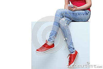 Girl with a smartphone in her hands sits on a white box. White isolate Stock Photo