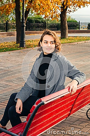 Girl smiling in gray coat sitting on bench in alley Stock Photo