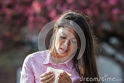 Girl sneezing in napkin in front of blooming tree in spring Stock Photo