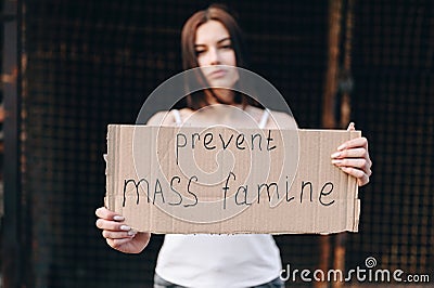 The girl is in soft focus, the focus is on cardboard inscription about the end of mass starvation Stock Photo