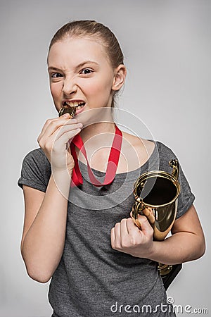 Girl in sportswear holding trophy and biting medal isolated on grey Stock Photo