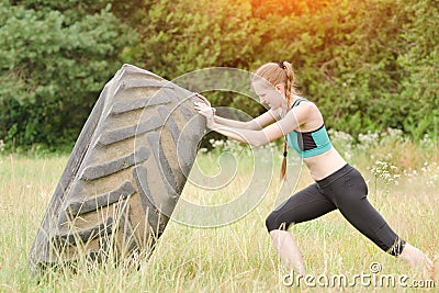 Girl in sportswear raises tire. Street workout. Stock Photo