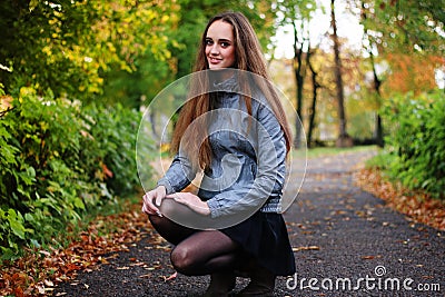 The girl squats in autumn wood in shining sun beams Stock Photo