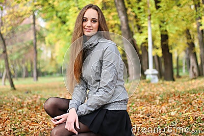 The girl squats in autumn wood in shining sun beams Stock Photo