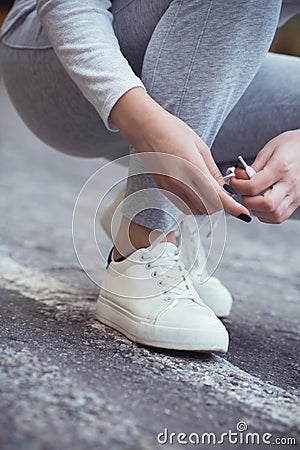 Girl squatted down to tie shoelaces on white sneakers on asphalt road, autumn sport concept outdoors Stock Photo