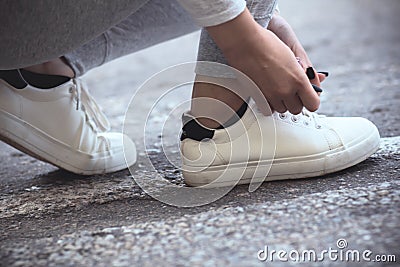 Girl squatted down to tie shoelaces on white sneakers on asphalt road, autumn sport concept outdoors Stock Photo