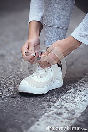 Girl squatted down to tie shoelaces on white sneakers on asphalt road, autumn sport concept outdoors Stock Photo