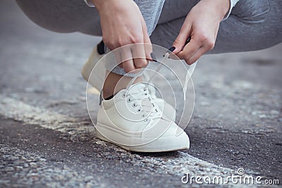 Girl squatted down to tie shoelaces on white sneakers on asphalt road, autumn sport concept outdoors Stock Photo