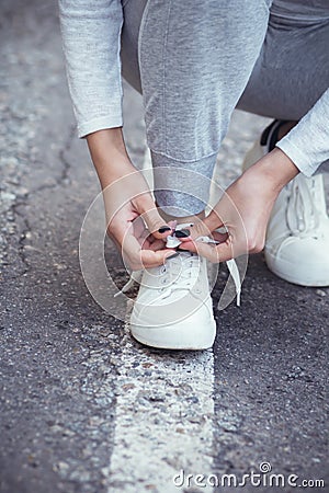 Girl squatted down to tie shoelaces on white sneakers on asphalt road, autumn sport concept outdoors Stock Photo