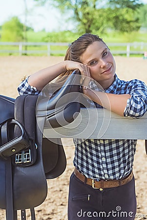 Girl Standing Behind The Wooden Fence In The Ranch - Saddle Hanging On The Fence Stock Photo