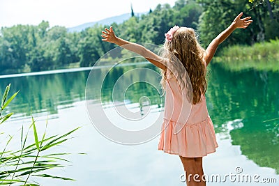 Girl standing at lakeside with open arms. Stock Photo