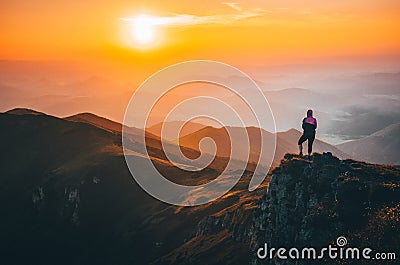 Girl standing on the top of the hill on the mountains meadow with beautiful colorful sunset over landscape Stock Photo