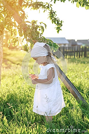 A girl standing under an apple tree in the sunlight. Barefoot baby in the garden Stock Photo