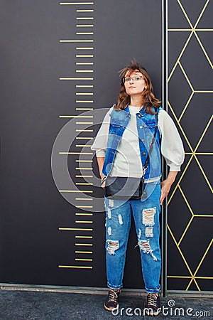 Girl stands next to a large scale ruler. Measurement of a woman in full growth. Man in denim near the wall with divisions Stock Photo