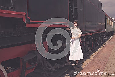 A girl stands on the steps of the cars train. The vintage train is at the station. Embarkation or disembarkation of the passenger Stock Photo