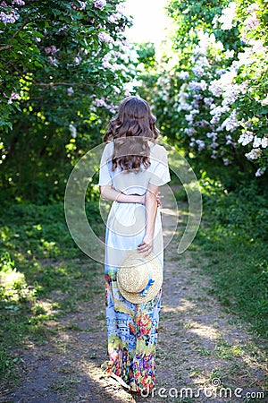 Girl in a straw hat with a blue ribbon on a spring afternoon. Back view. Trendy casual summer or spring outfit. Street fashion. Wo Stock Photo