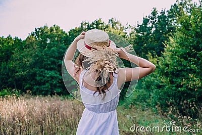 Girl in a straw hat with her back to the photographer. Girl in a white dress on a summer sunny day. Stock Photo
