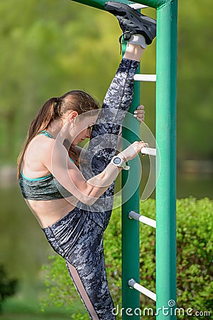 Girl on the street workout. She pulls up her leg on parallel rails. The girl does the splits. She is dressed in a gray T-shirt and Stock Photo